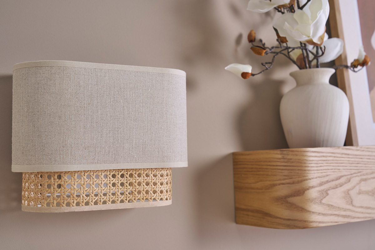Applique murale en lin beige et cannage rotin, vue de c�t�, avec vase en arri�re-plan.