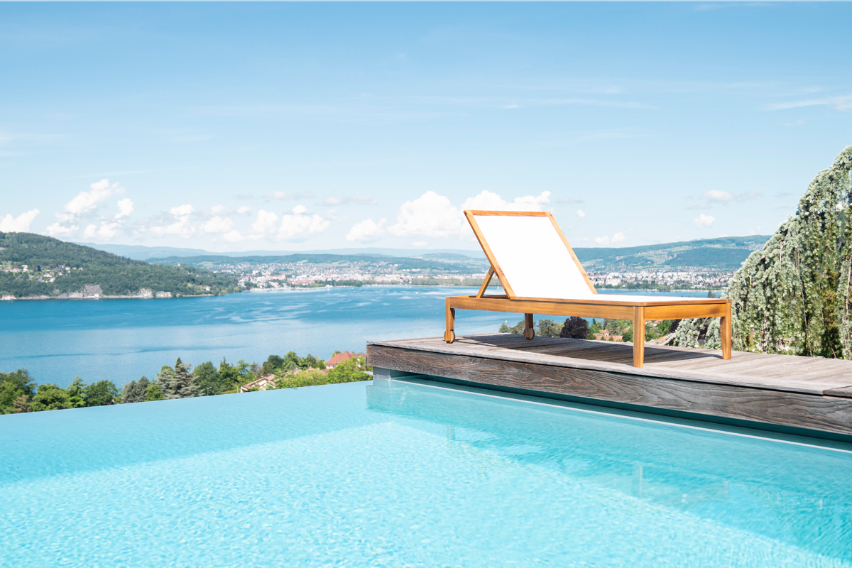 Bain de soleil blanc NAVEEN en bois massif au bord d'une piscine, vue sur lac.