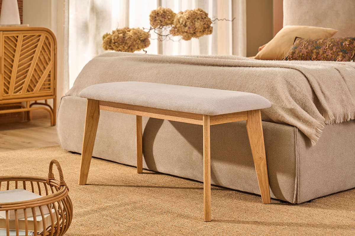 Banc scandinave beige et bois clair devant un lit dans une chambre.