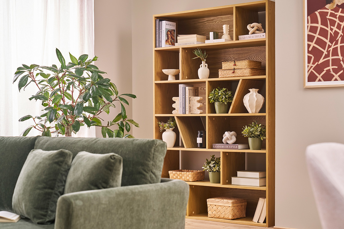 Biblioth�que en bois clair avec rangements asym�triques, d�cor�e de livres et plantes, vue de c�t�.