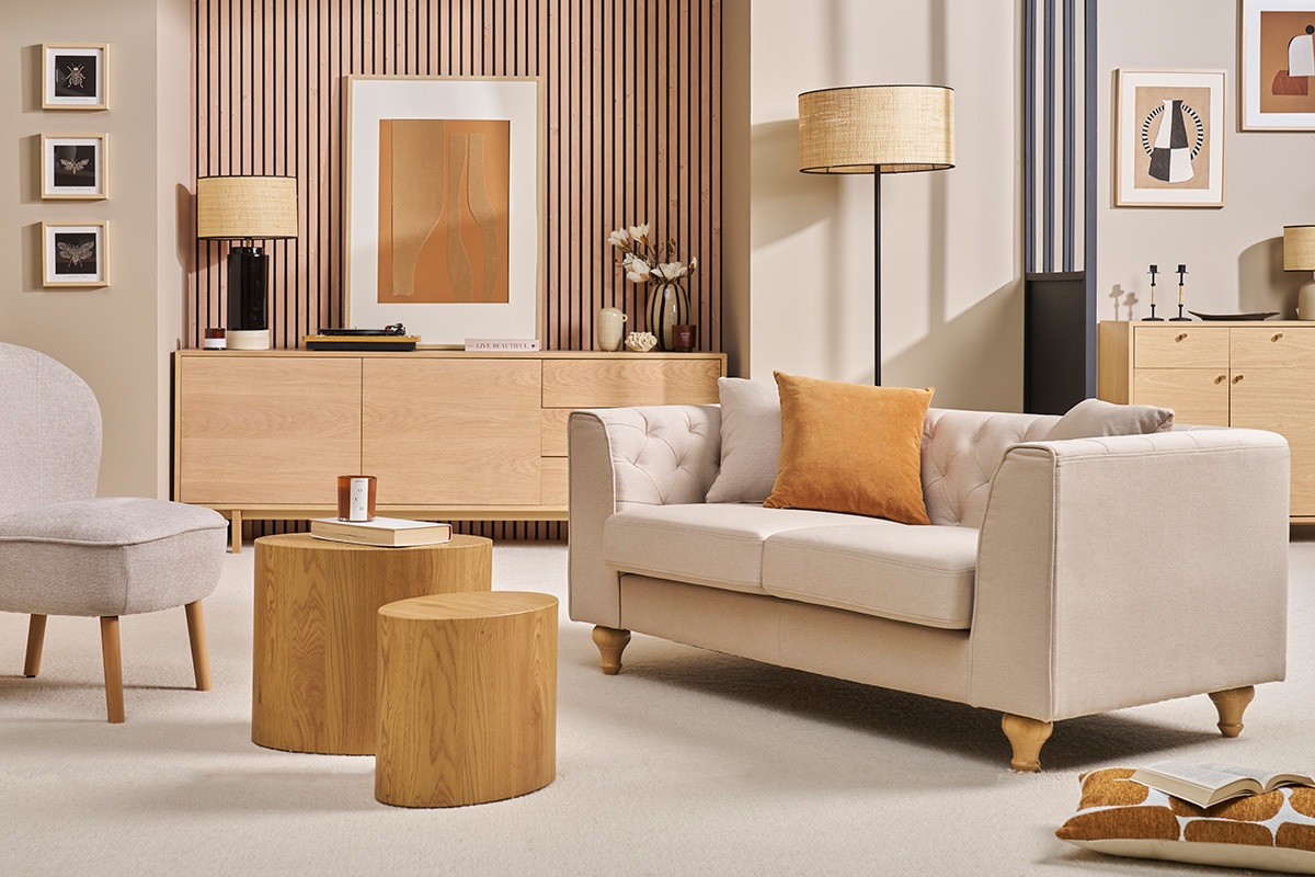 Canap� 2 places capitonn� beige MONTAIGNE en tissu, vue de c�t� avec coussin orange, dans un salon �l�gant.