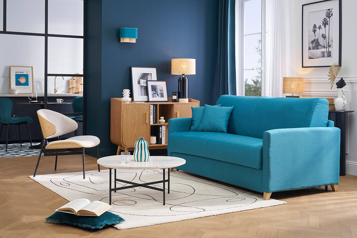 Salon avec canap� convertible bleu canard, vue face, table basse ronde, et fauteuil bois clair.