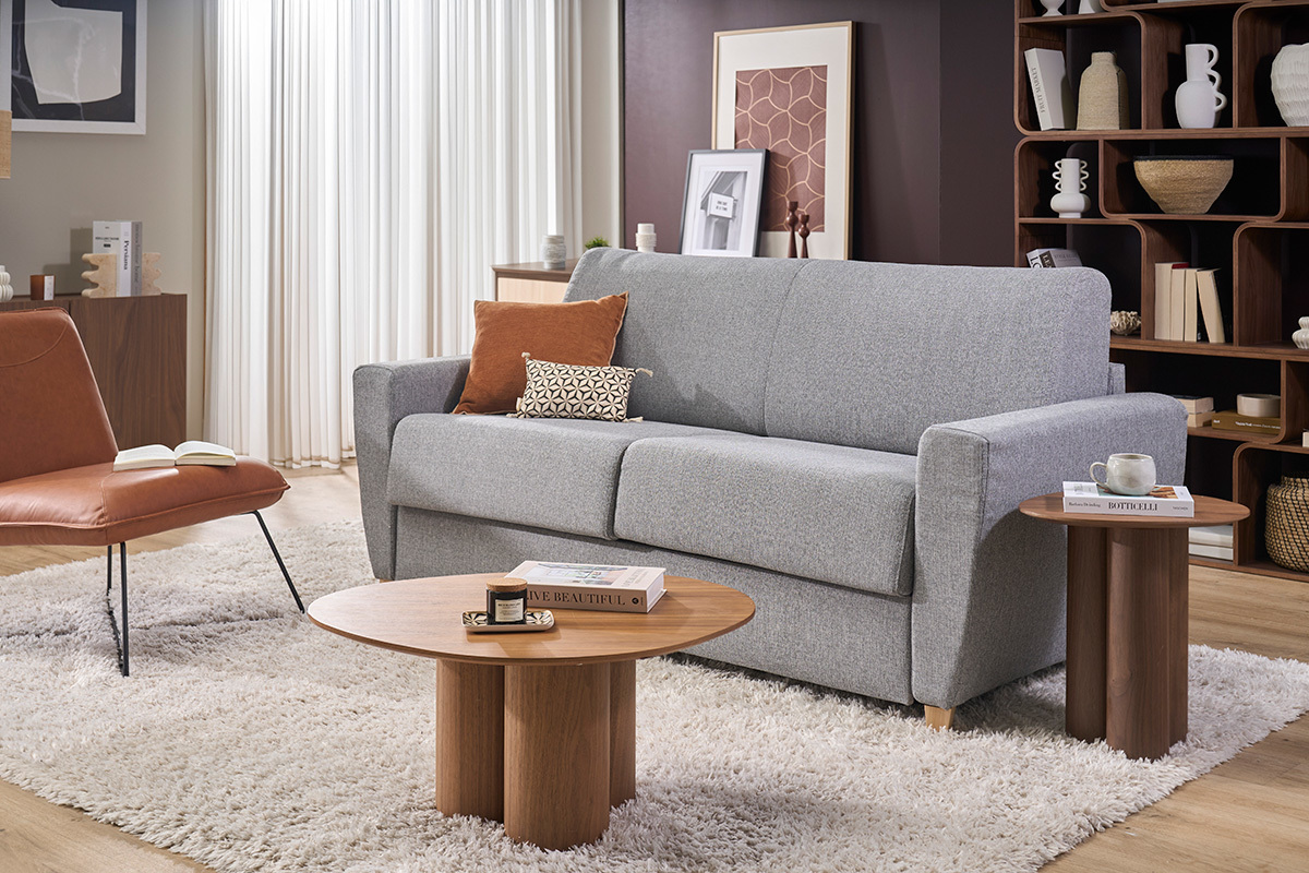 Canap� convertible GRAHAM en tissu gris clair avec coussins, accompagn� de tables basses, vue de face.