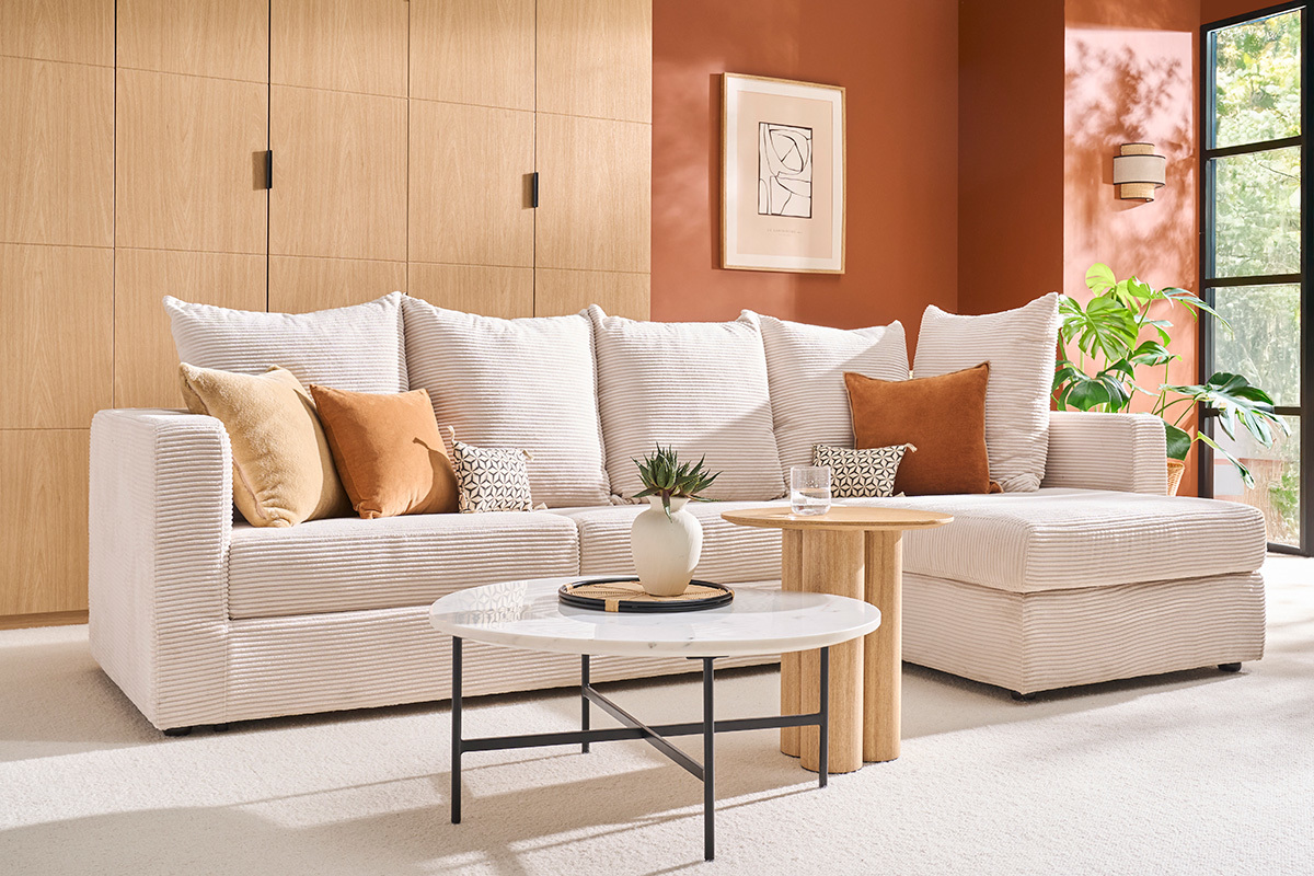 Canap� d'angle convertible beige en velours c�tel� avec coussins, table basse en marbre, vue de c�t�.