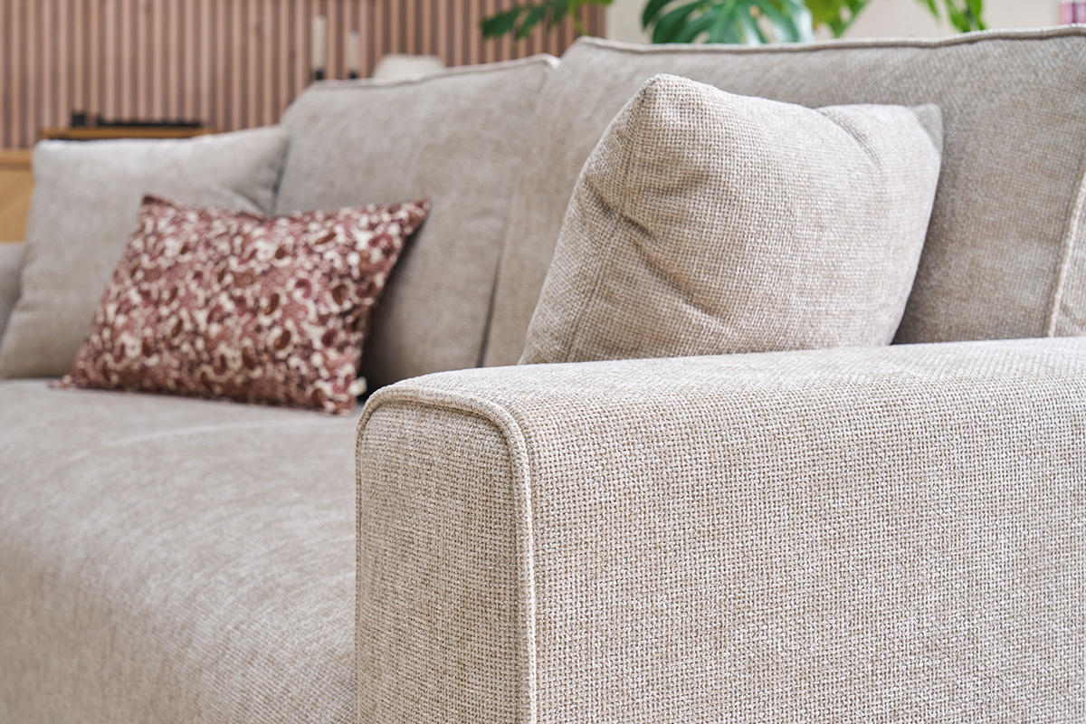 Canap� beige effet velours textur�, accoudoir et coussins visibles, vue de c�t�.