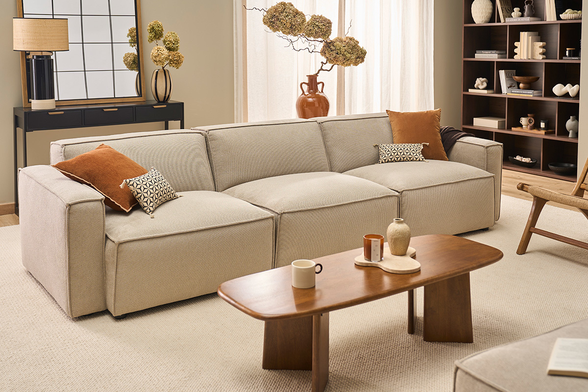 Canap� modulable 4 places beige effet velours textur�, dans un salon moderne avec table en bois et coussins.