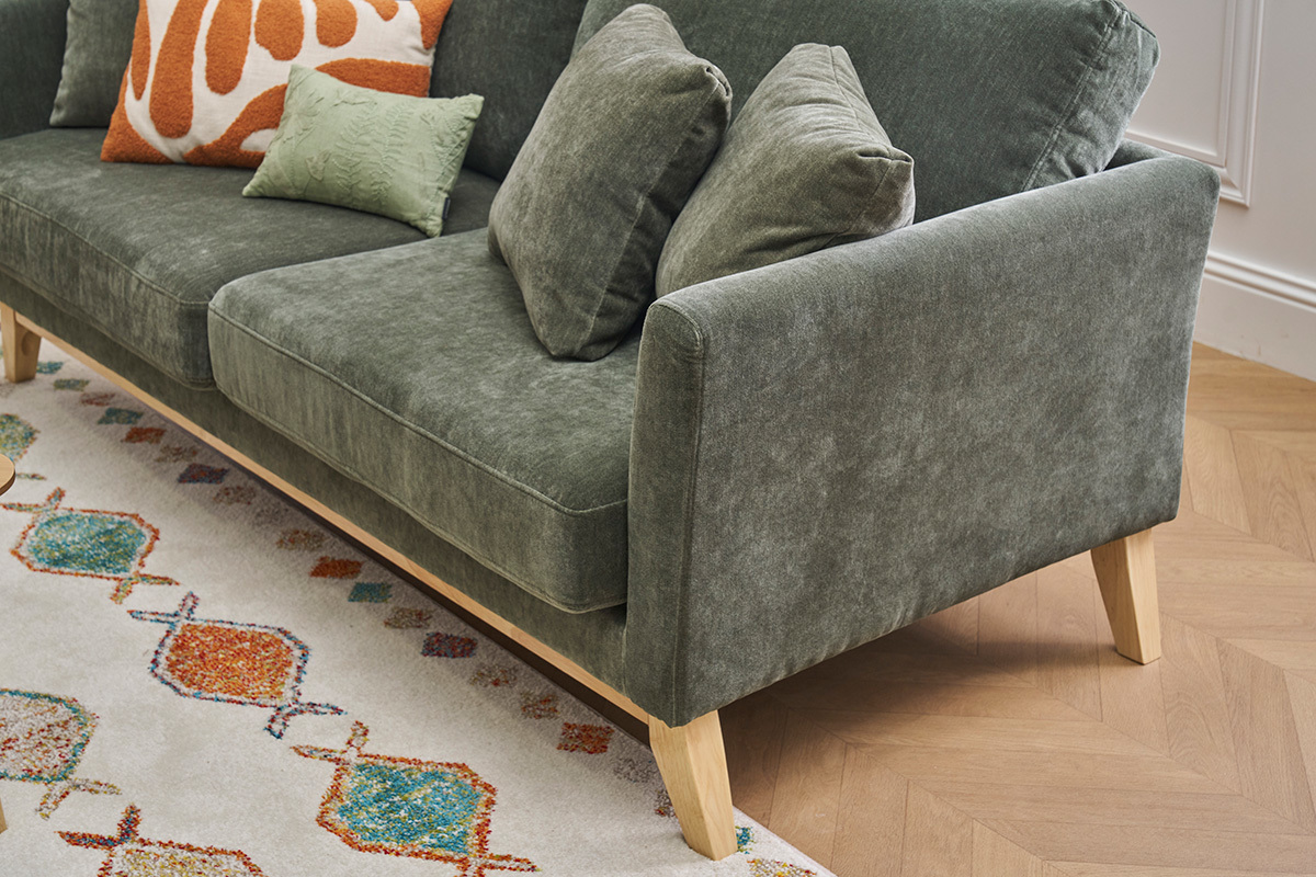 Canap� 3 places vert kaki en tissu et bois, vue d'angle avec coussins, sur parquet et tapis color�s.