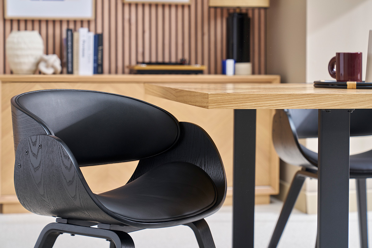 Chaise design noire BENT avec dossier en bois, vue de profil � c�t� d'une table en bois clair.