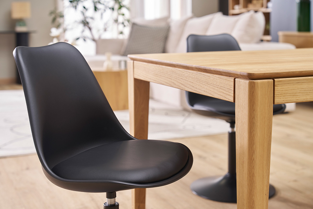 Chaise pivotante noire STEEVY V2 pr�s d'une table en bois, vue 3/4.