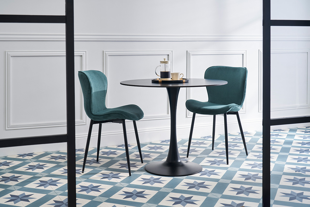 Deux chaises en velours c�tel� bleu canard avec pieds en m�tal noir autour d'une table noire.