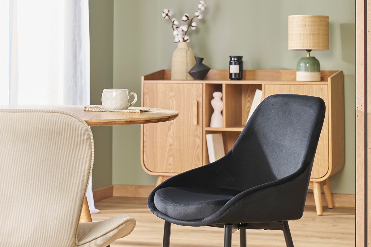 Chaise design noire en velours et m�tal pr�s d'une table et d'un buffet en bois.