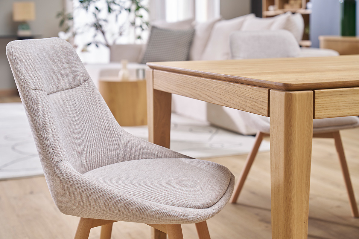 Chaise en tissu effet velours beige et bois clair � c�t� d'une table en bois.