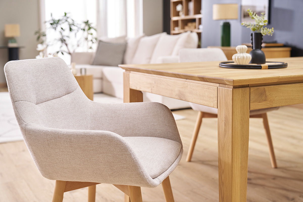 Chaise en tissu effet velours beige avec pieds en bois clair, vue pr�s d'une table en bois.