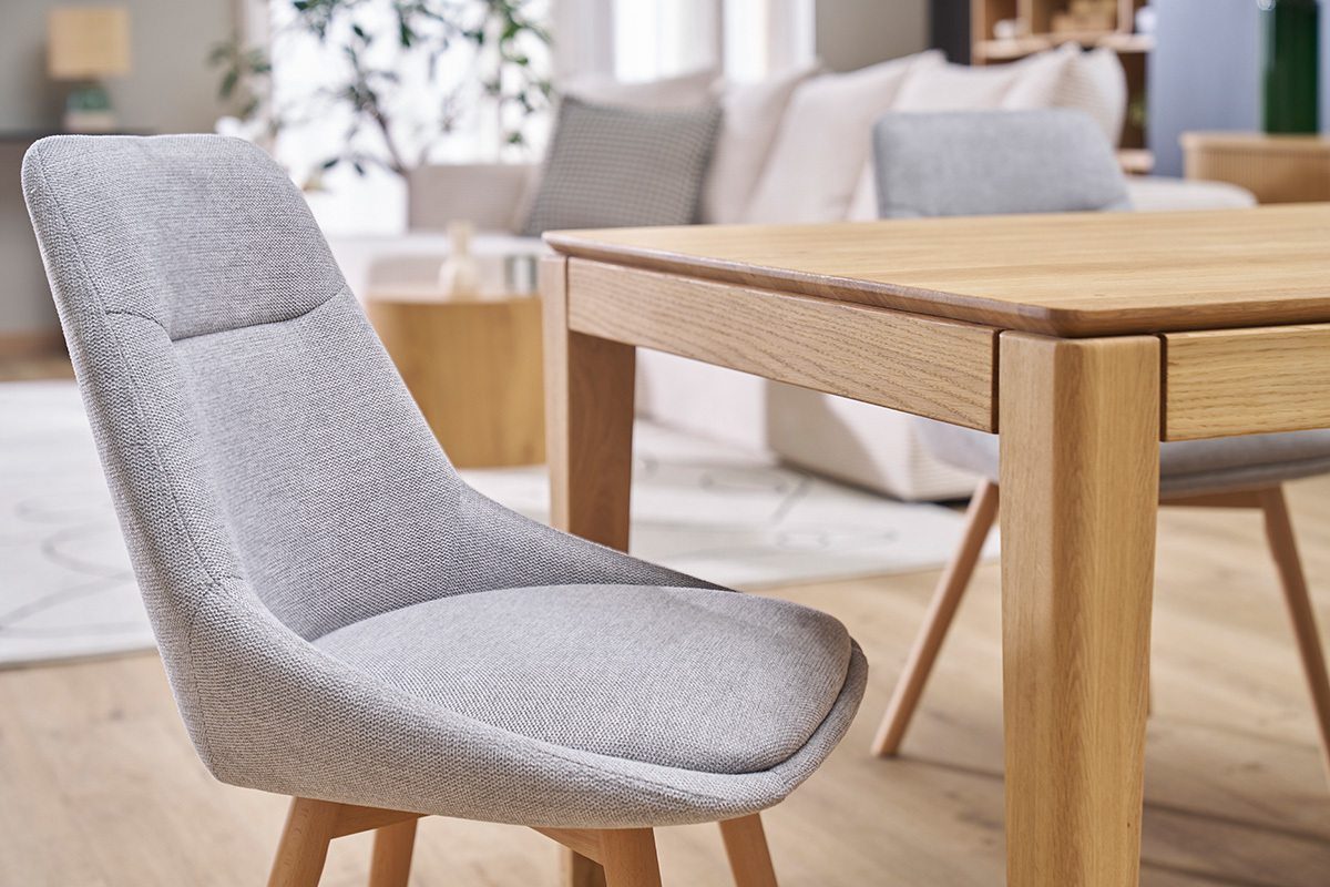 Chaise en tissu effet velours gris clair avec pieds en bois clair, vue de profil pr�s d'une table.