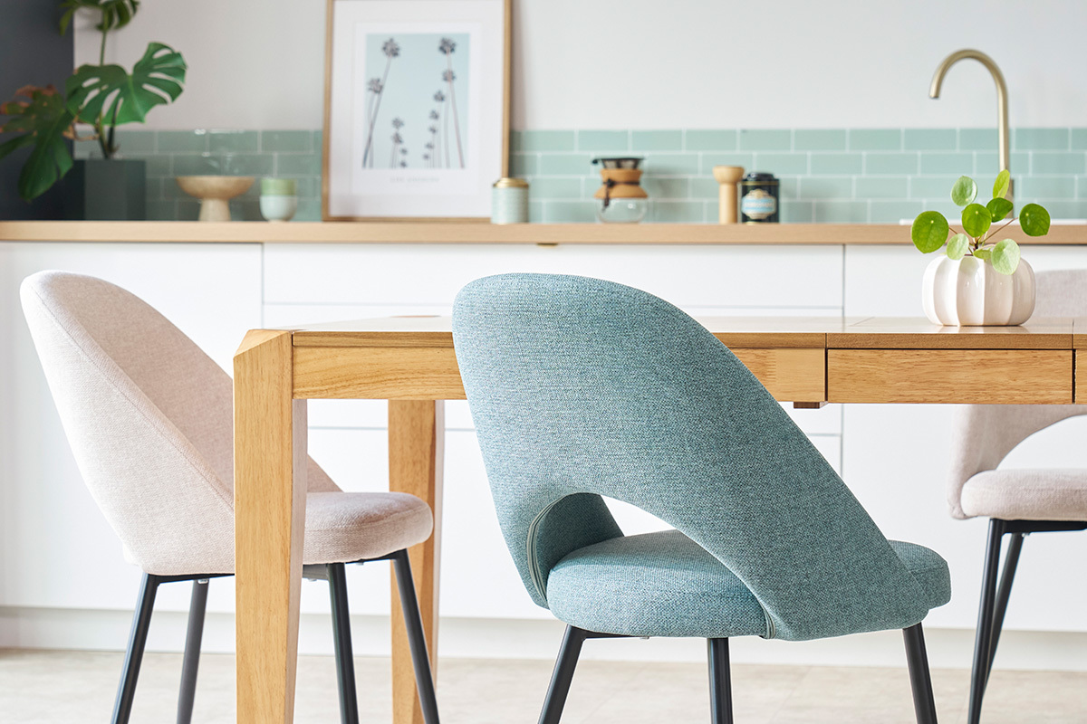 Chaises vintage vert de gris en tissu, pieds en m�tal noir, autour d'une table en bois dans une cuisine moderne.