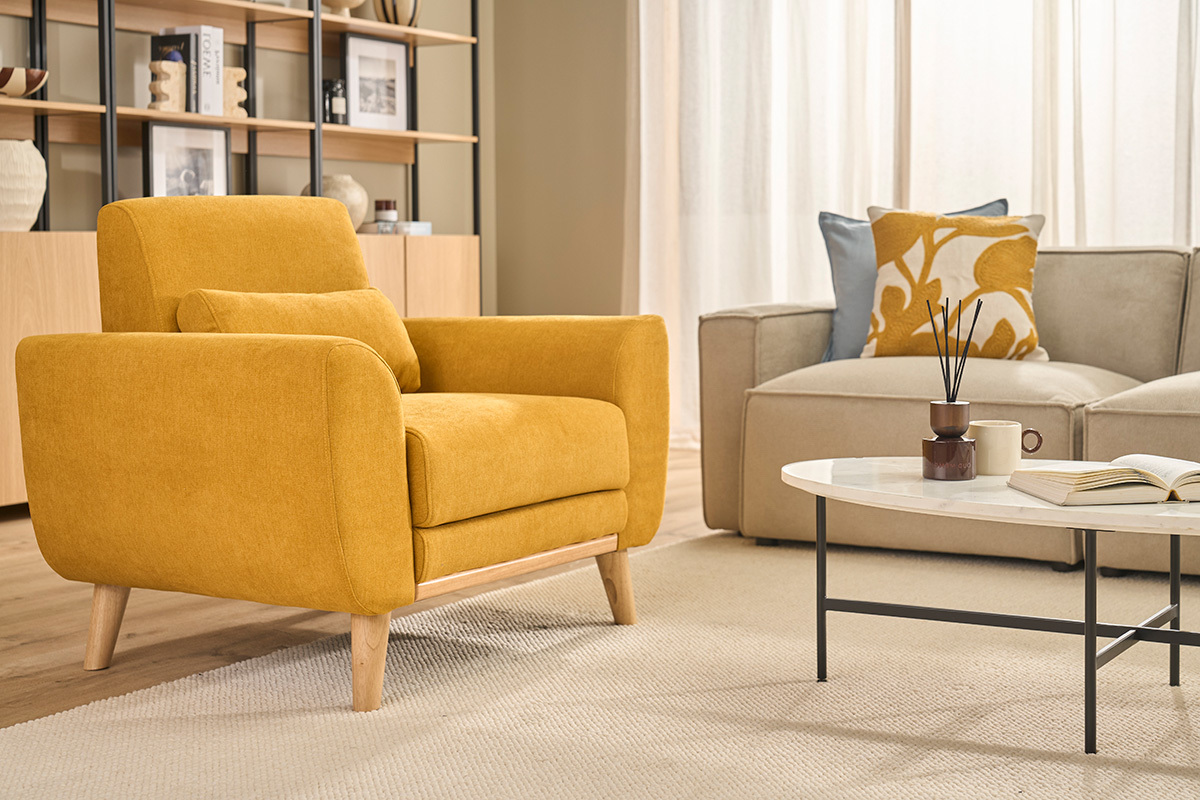Fauteuil scandinave jaune moutarde en tissu effet velours, vue de profil, avec coussin sur un tapis.