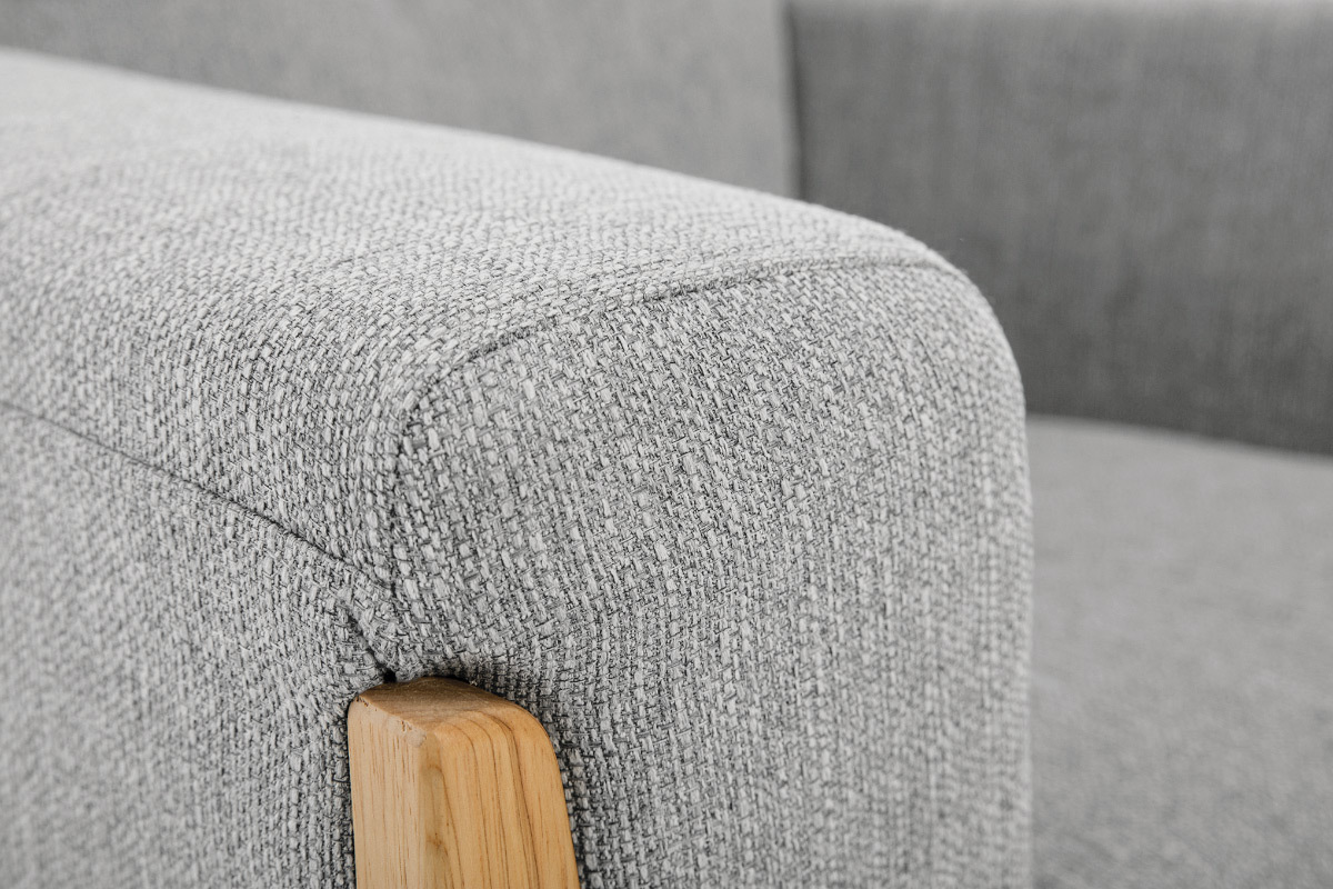 Gros plan sur le tissu gris et l'accoudoir en bois clair du fauteuil scandinave FJORD.