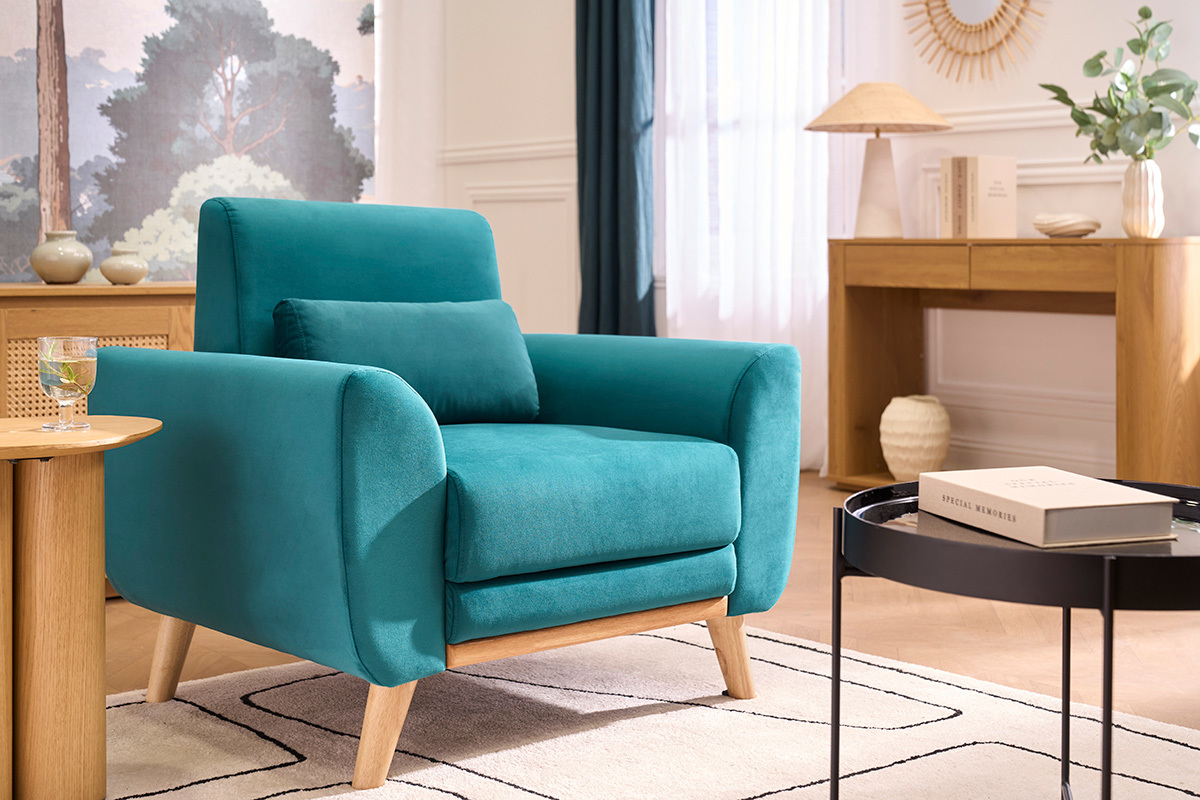 Fauteuil scandinave en velours bleu p�trole avec accoudoirs et coussin, devant un meuble en bois clair.