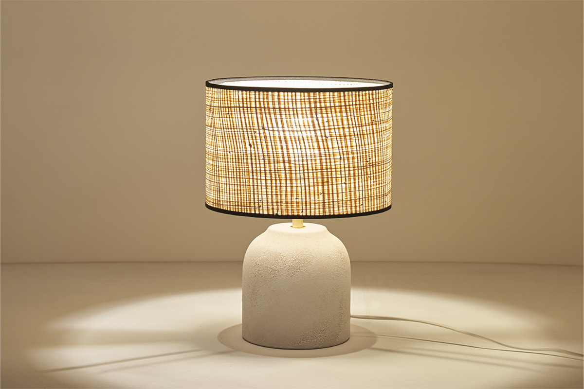 Lampe en c�ramique blanche allum�e avec abat-jour en raphia, vue de face.