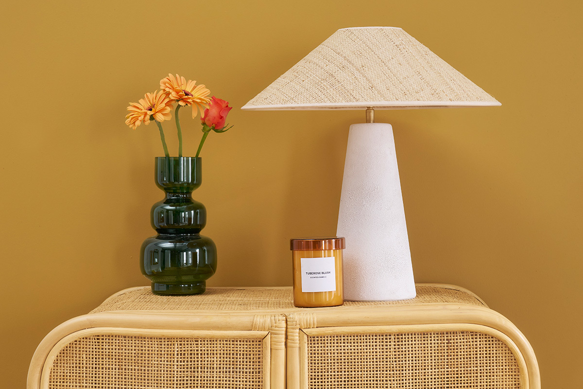 Lampe � poser JUNI avec pied en c�ramique blanc et abat-jour en rabane sur meuble en osier.