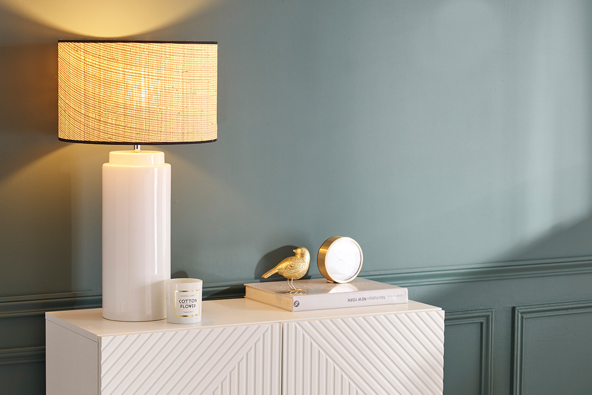 Lampe en c�ramique blanche avec abat-jour en raphia naturel sur buffet blanc, vue de face.