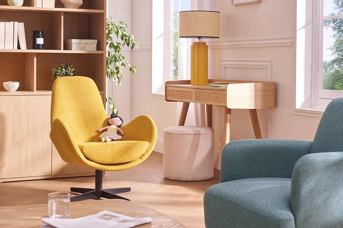 Lampe en c�ramique jaune avec abat-jour en raphia sur une table en bois, fauteuils color�s autour.