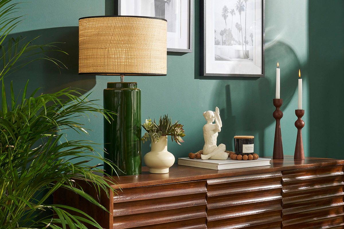 Lampe � poser verte en c�ramique avec abat-jour en raphia sur un buffet, accessoires d�coratifs autour.