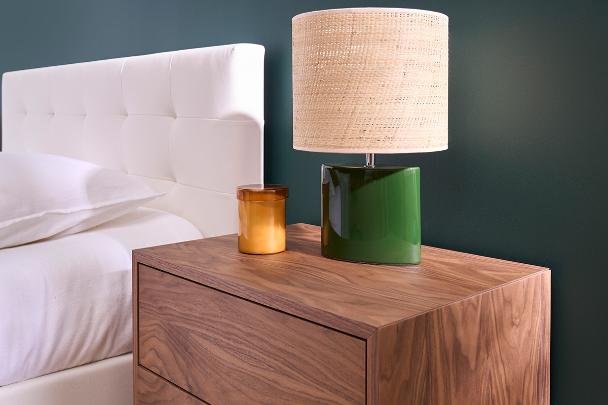 Lampe � poser en c�ramique vert fonc� avec abat-jour en raphia sur un meuble en bois, vue de profil.