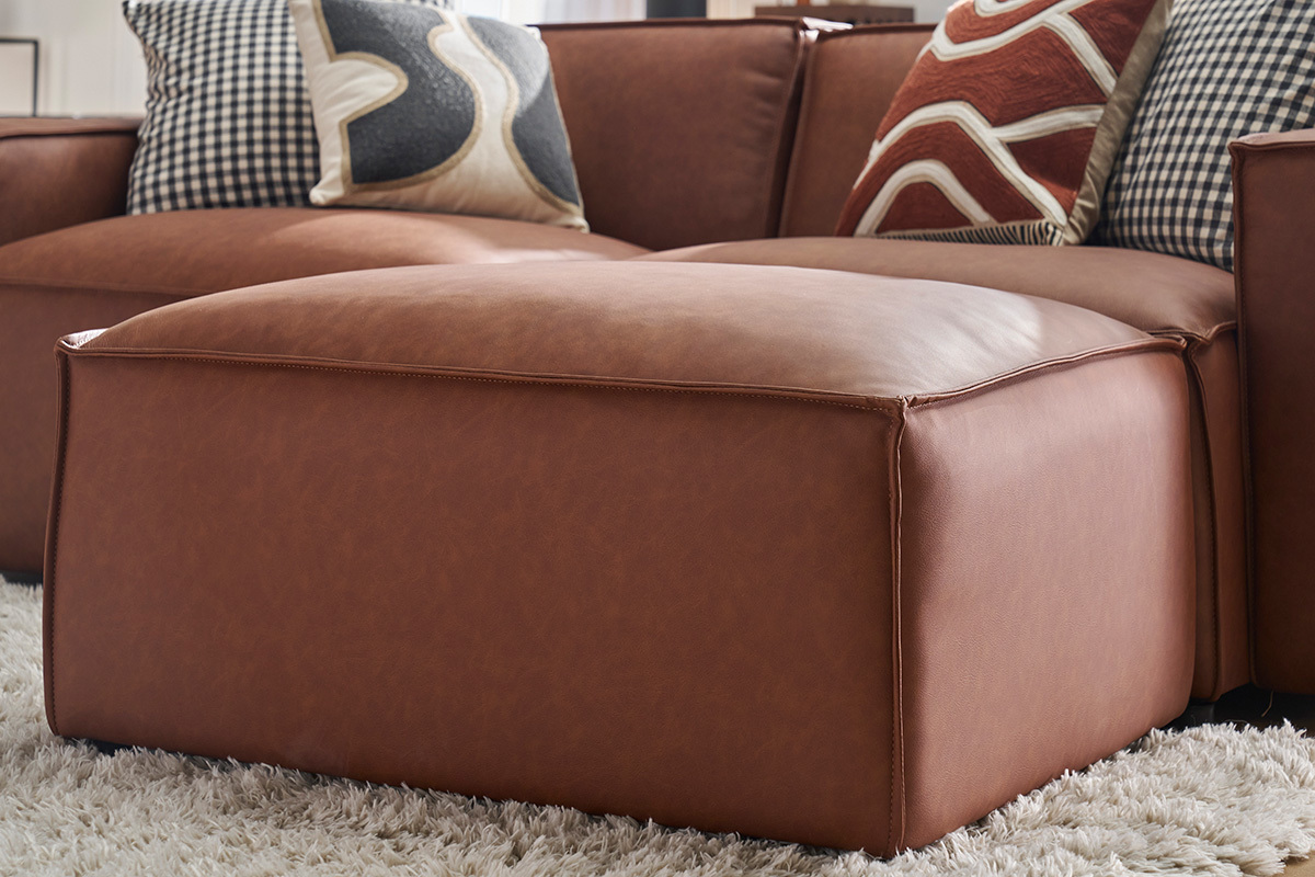 Pouf repose-pieds en cuir marron devant un canap�, vue zoom�e.