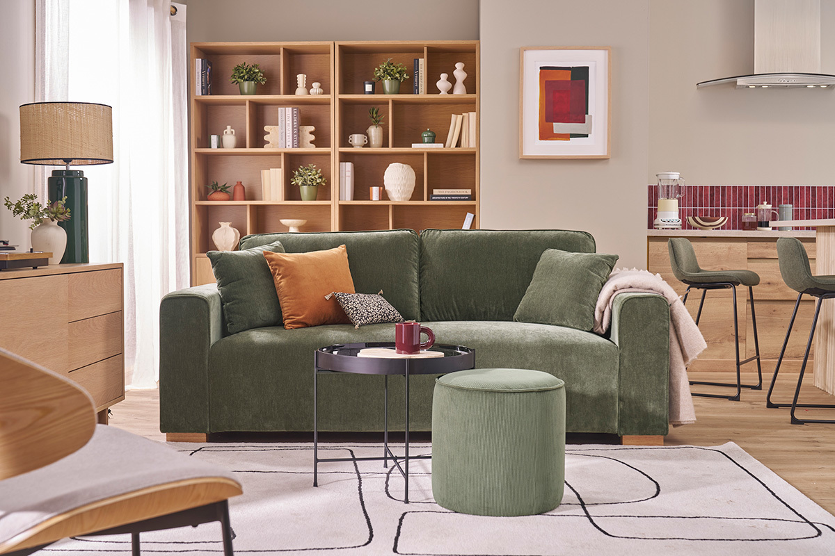 Pouf rond en velours c�tel� vert kaki devant un canap� dans un salon.