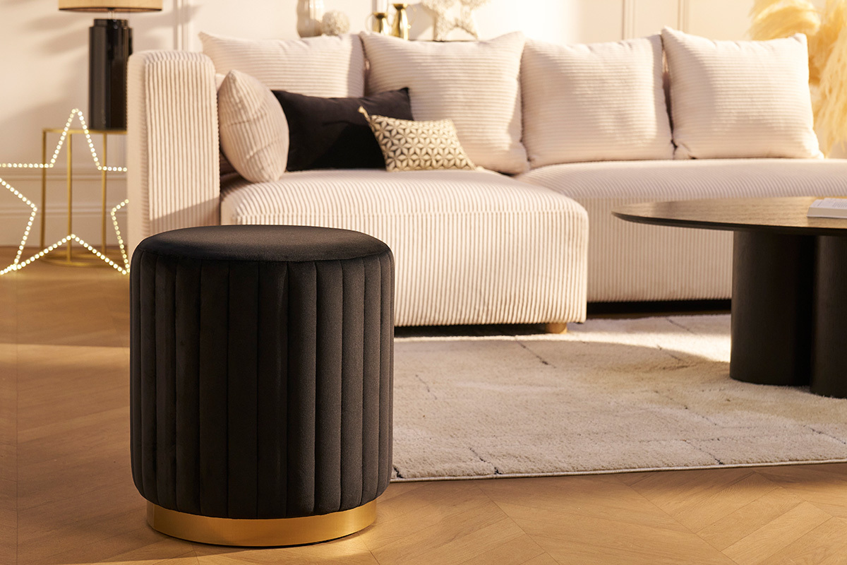 Pouf rond en velours noir et m�tal dor� devant un canap� beige.