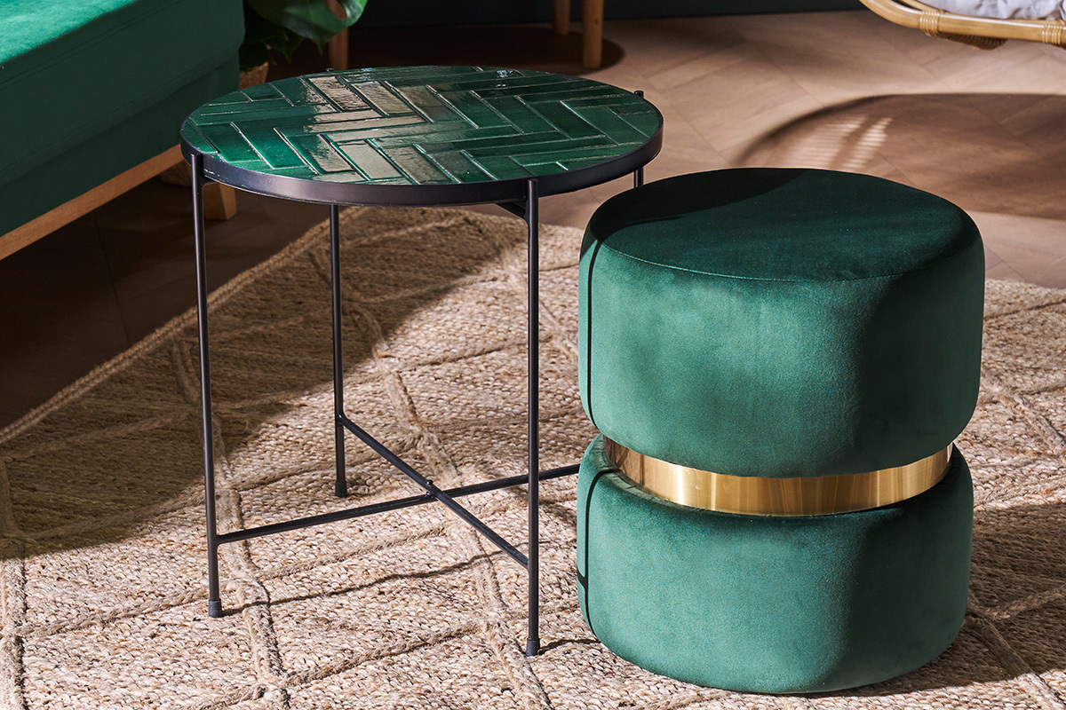 Pouf rond en velours vert fonc� et m�tal dor� � c�t� d'une table sur tapis clair.