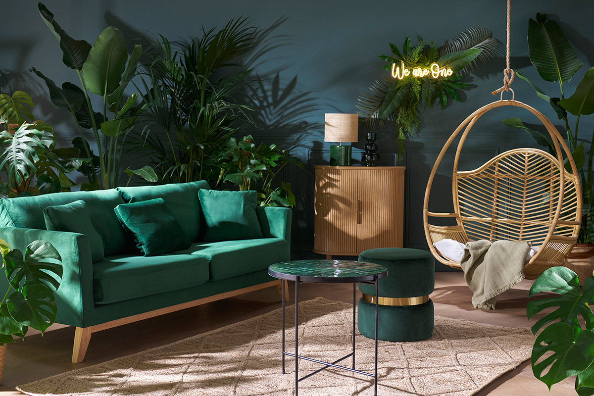 Salon avec pouf rond en velours vert fonc� et m�tal dor�, pr�s d'un canap� vert.