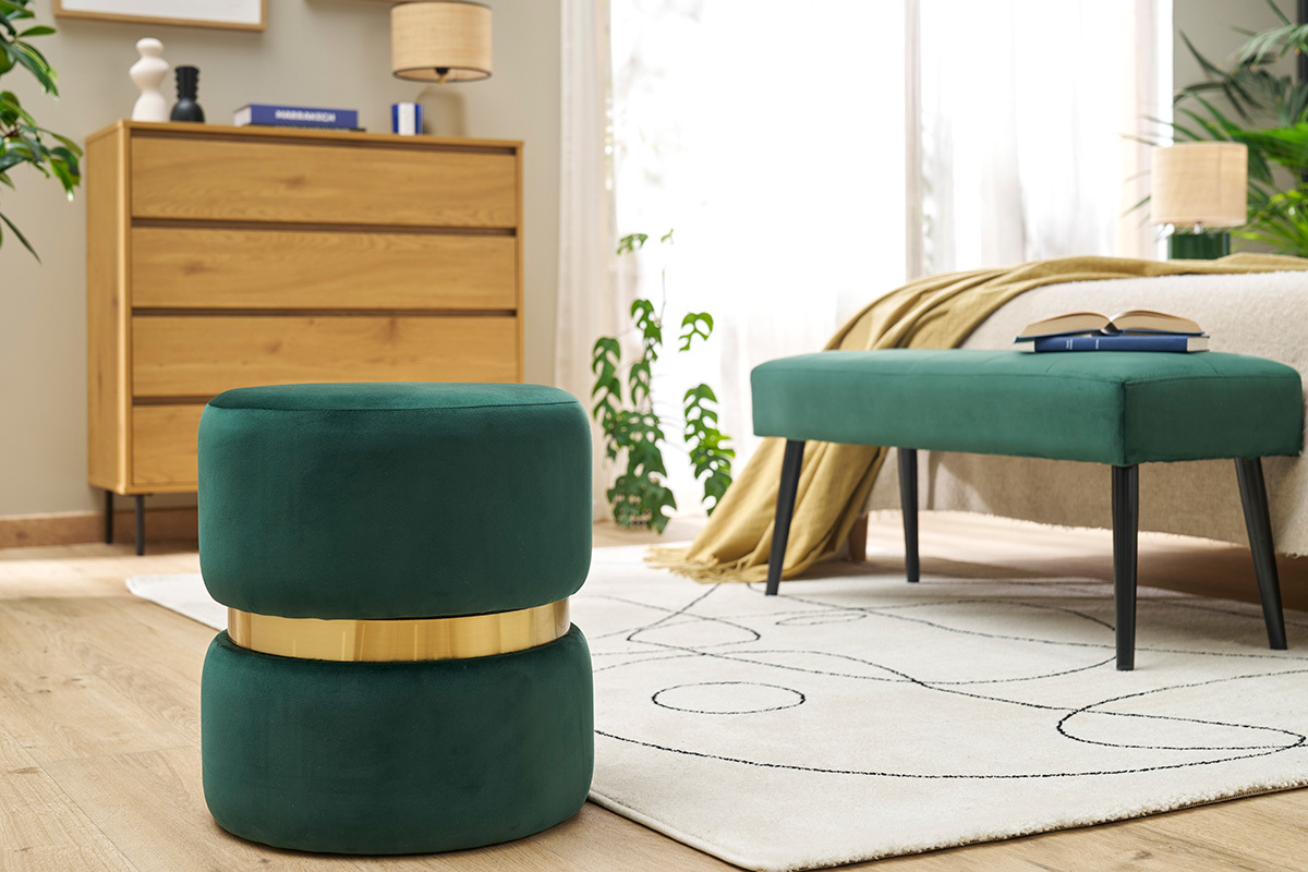Pouf rond en velours vert fonc� avec bande dor�e, pos� dans un salon moderne.