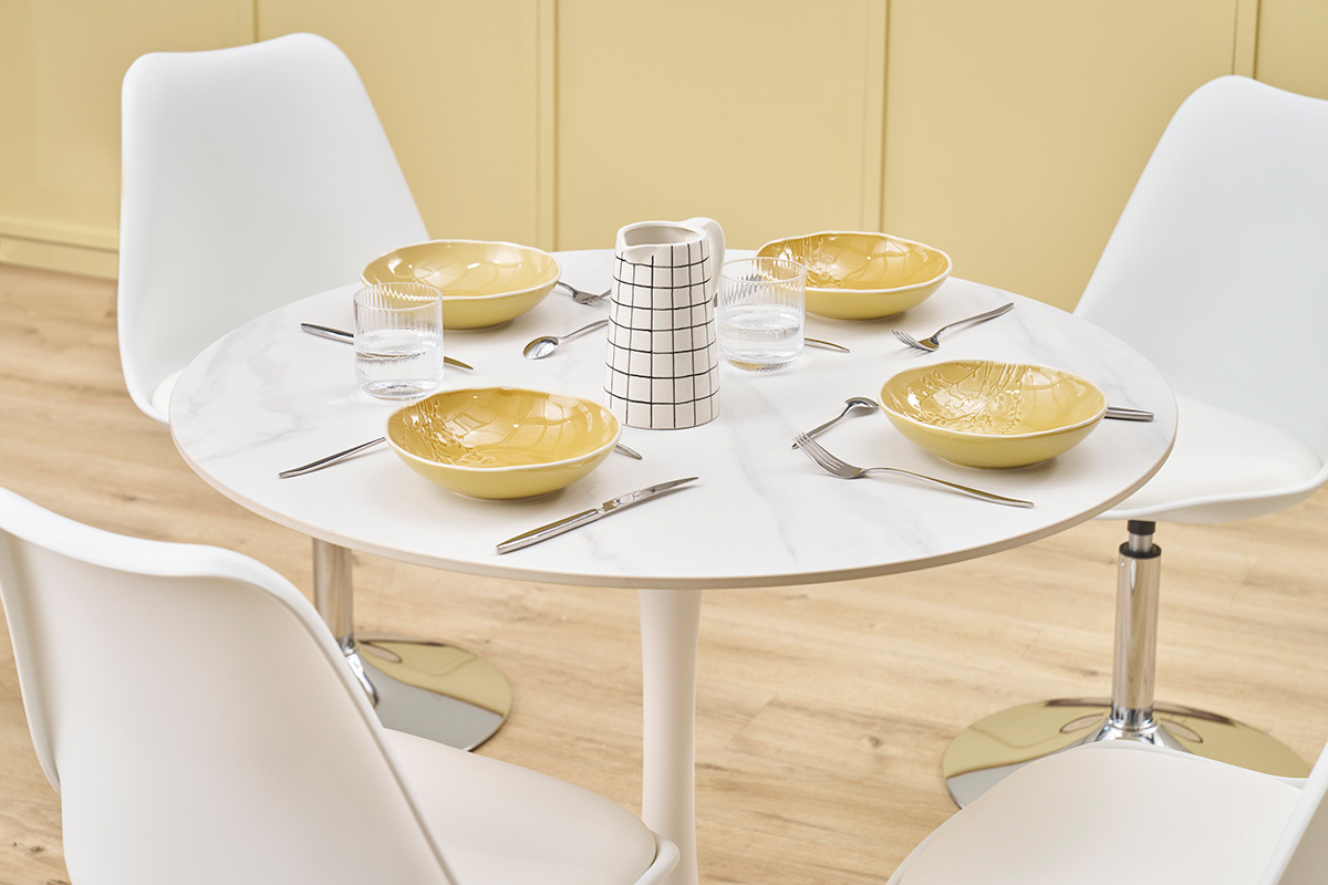 Table ronde en c�ramique blanche, couverts, assiettes jaunes, verres et carafe.
