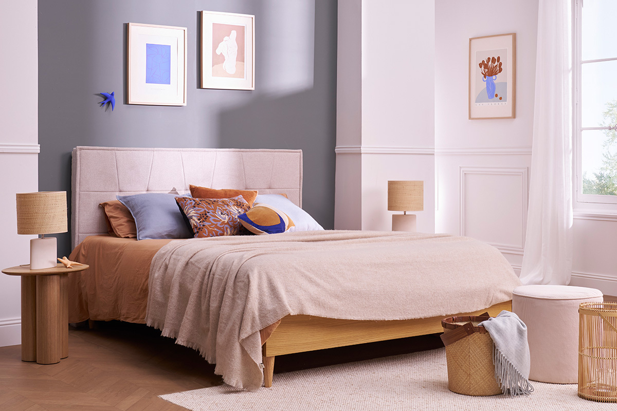 Table d'appoint HOLLEN en bois clair pr�s d'un lit dans une chambre avec lampes et accessoires d�co.
