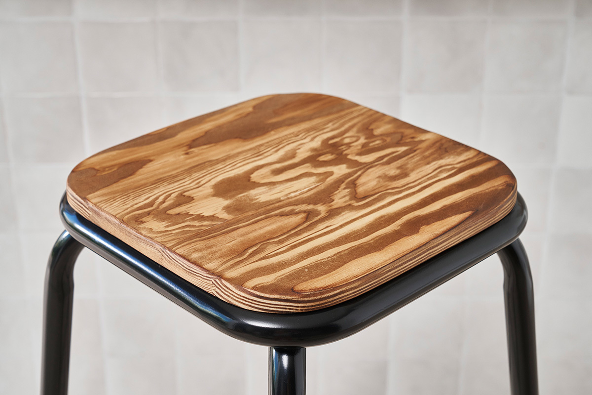 Gros plan sur l'assise carr�e en bois d'un tabouret de bar empilable avec structure en m�tal noir.